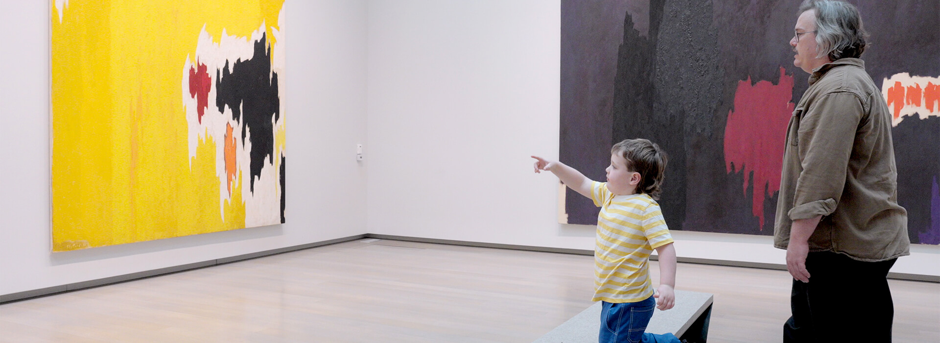 A child kneels on a bench and points at a painting