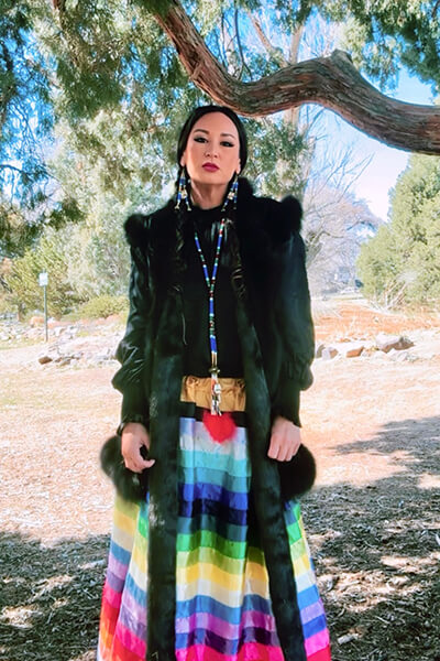 A woman wearing a colorful skirt stands in front of a tree outside