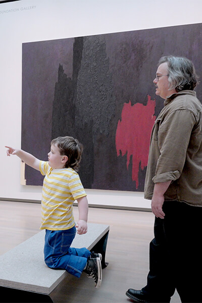 A child kneels on a bench and points at a painting
