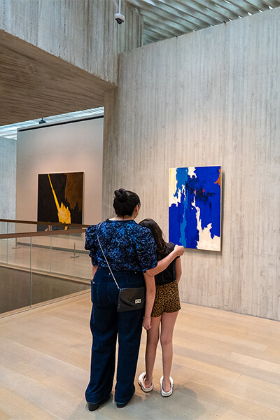 A woman and her daughter look at a blue painting