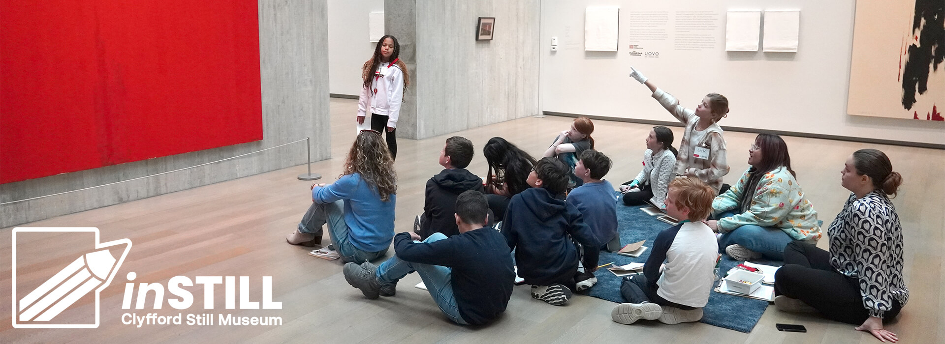 A school field trip group sits on the floor of the Clyfford Still Museum while one student stands up near a painting