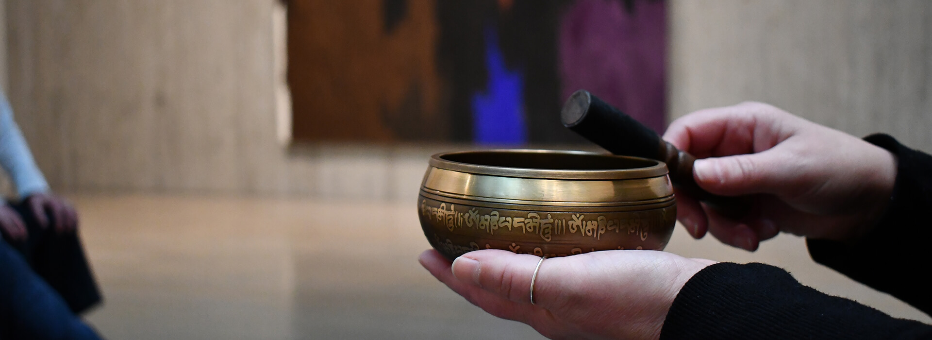 Closeup of hands holding a meditation bowl in front of a painting