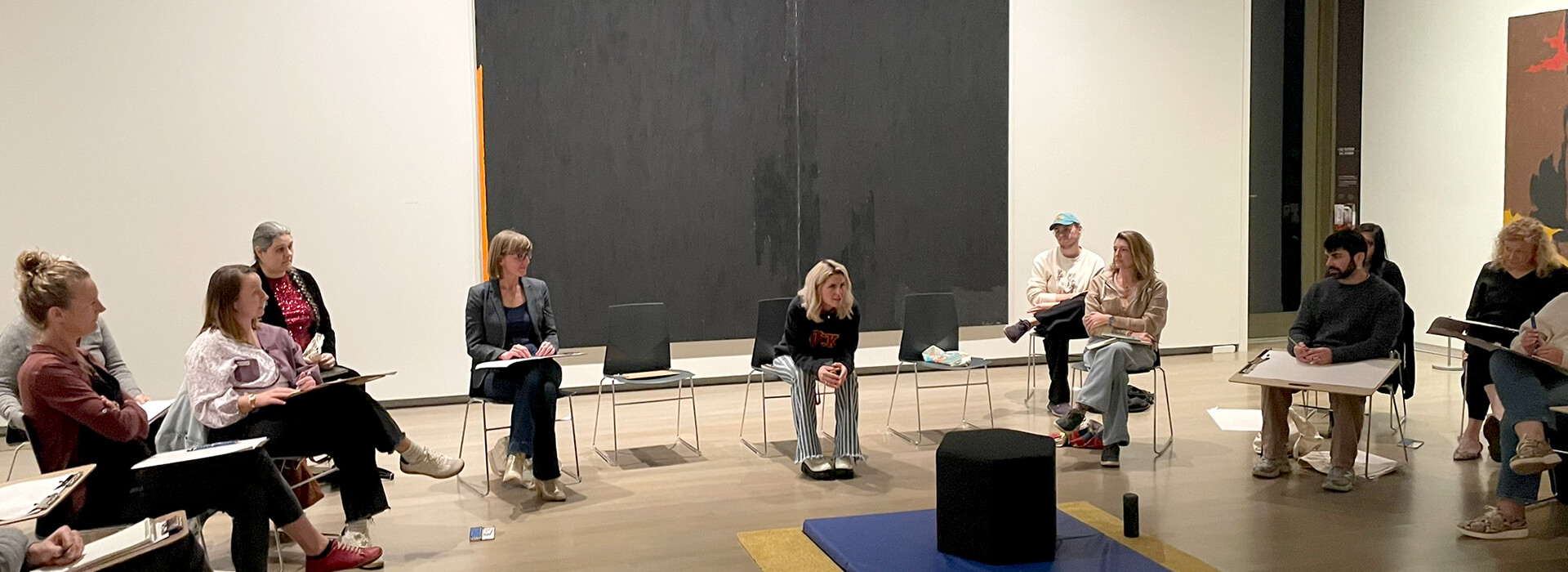 A woman sits in a chair teaching a workshop to others listening to her