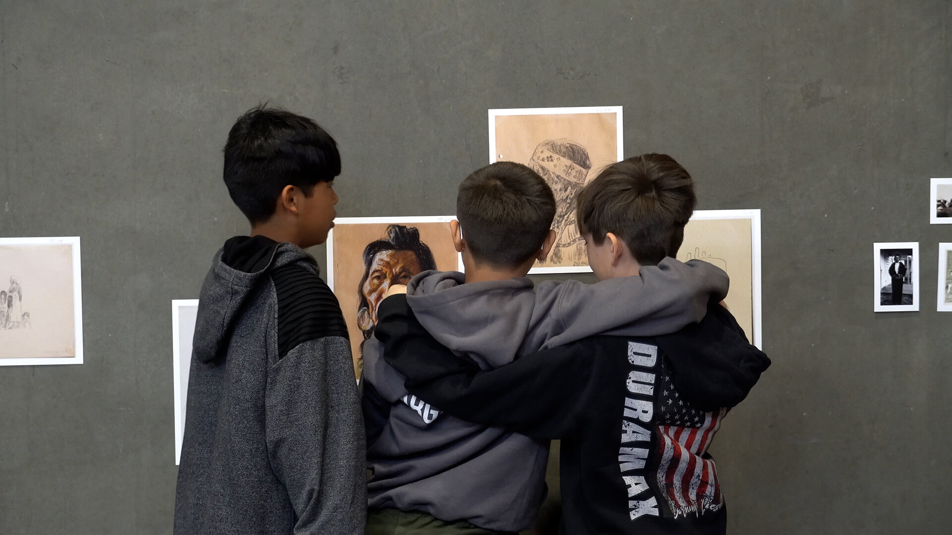 Three boys look at artwork reproductions on a gray wall