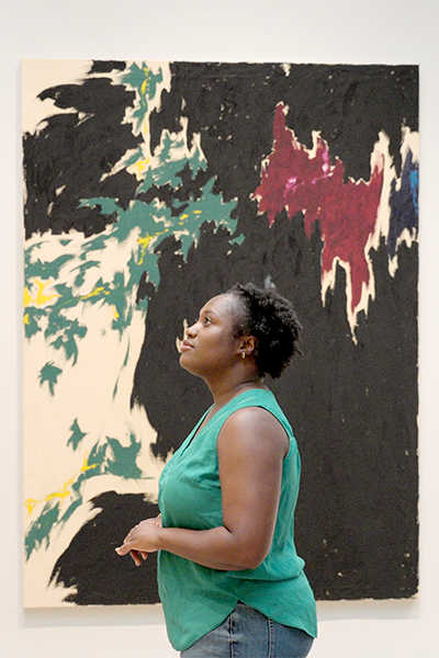 A woman stands in front of a colorful abstract painting
