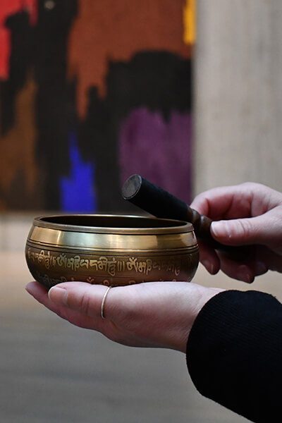 Closeup of hands holding a meditation bowl in front of a painting