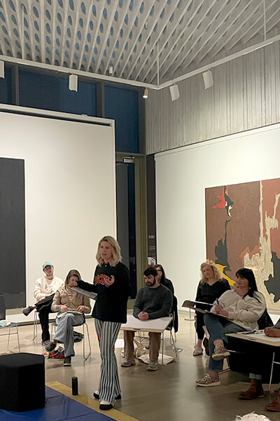 A woman stands and teaches an artmaking workshop