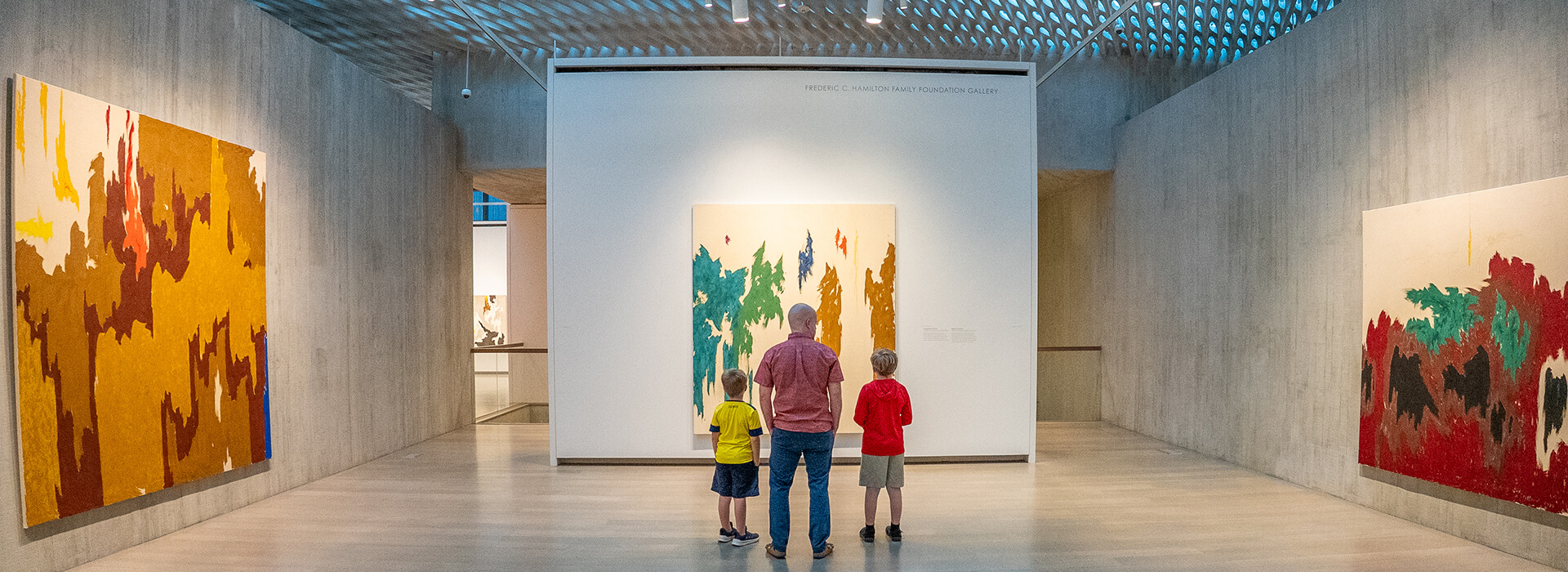 A father and his sons look at a large colorful abstract painting