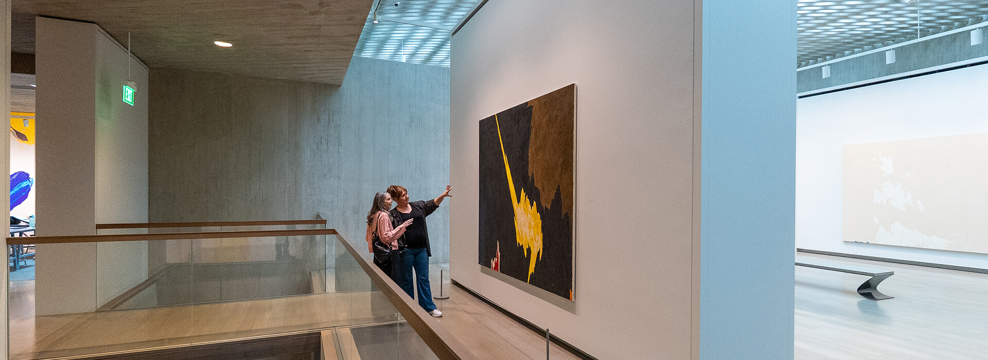 Two women look at a painting on the back wall of a gallery