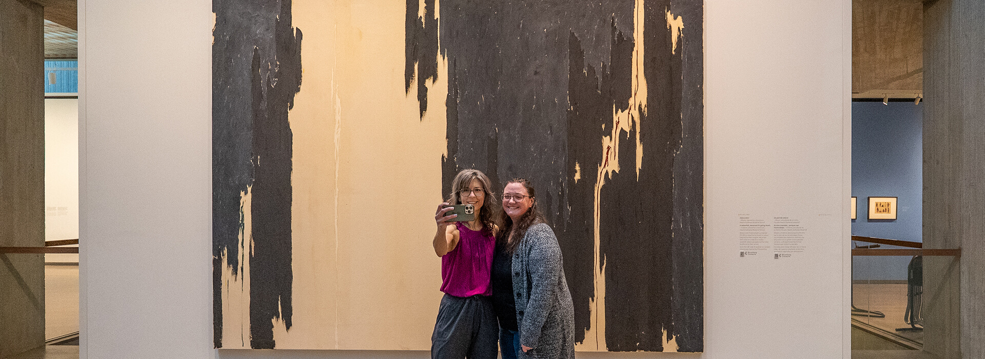 Two women take a selfie in front of a large painting