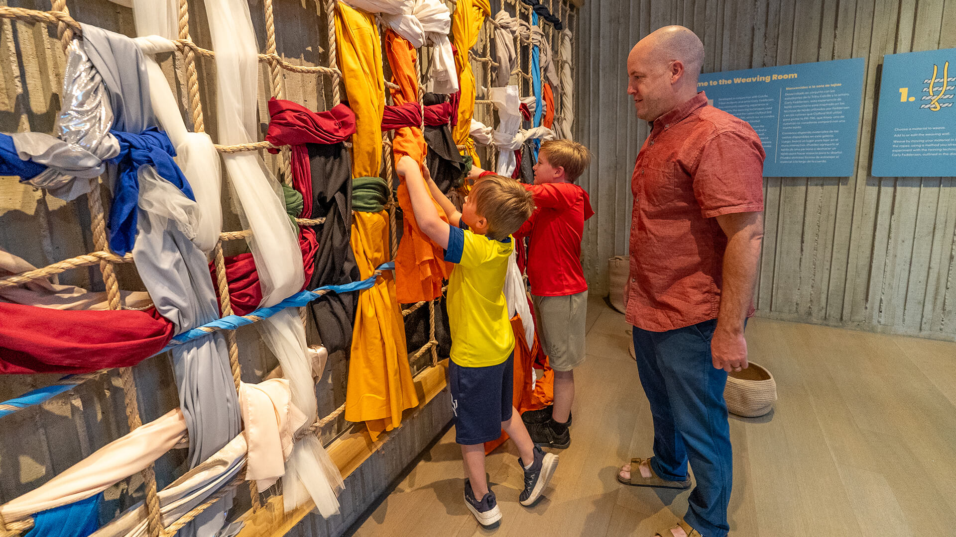 A father and his sons play with an interactive weaving wall