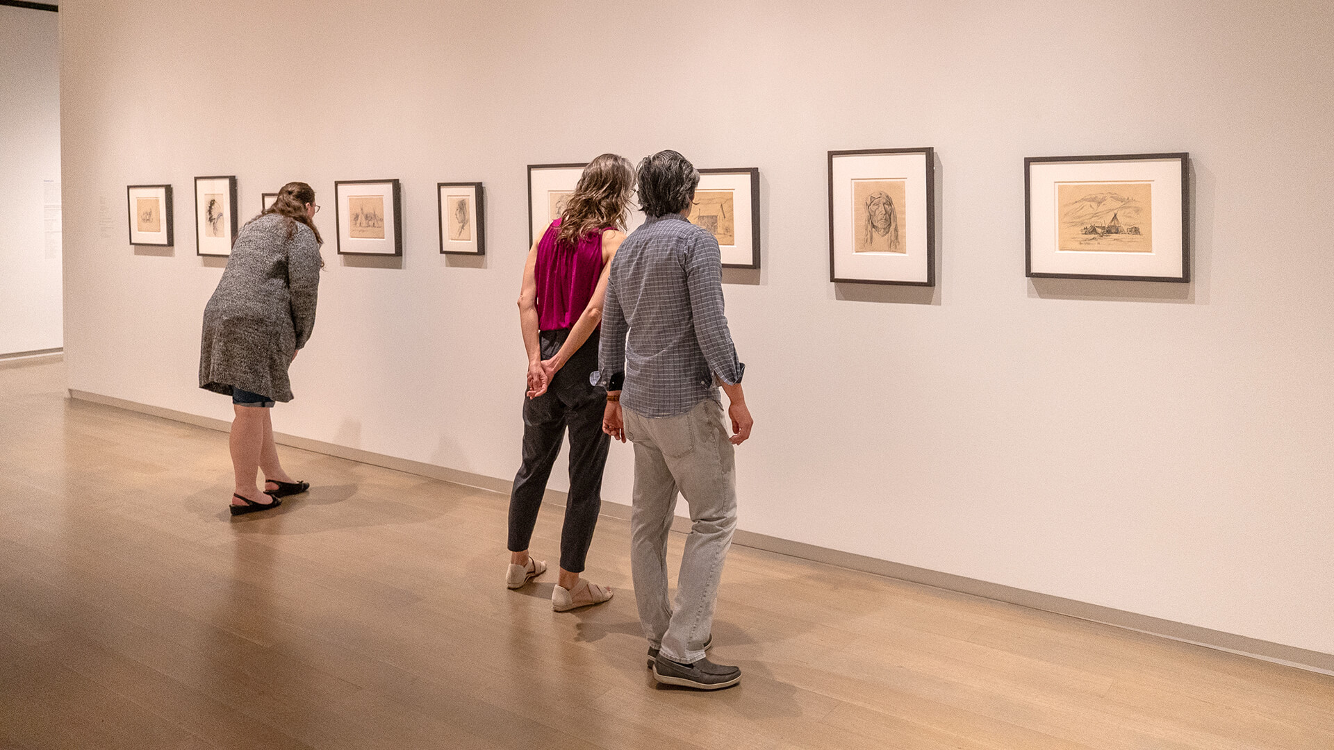 Three people look at small framed artworks on the wall