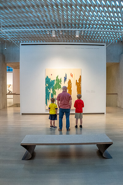 A father and his sons look at a large colorful abstract painting