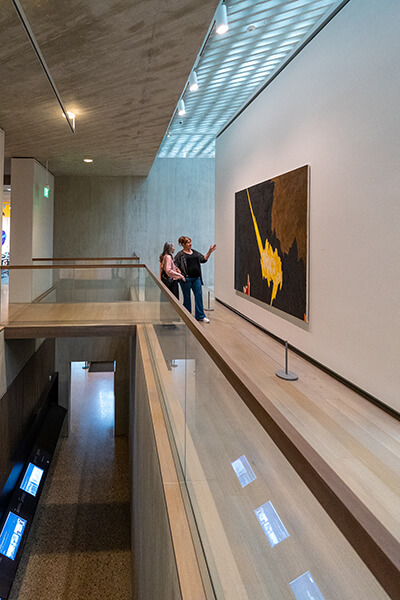 Two women look at a painting on the back wall of a gallery