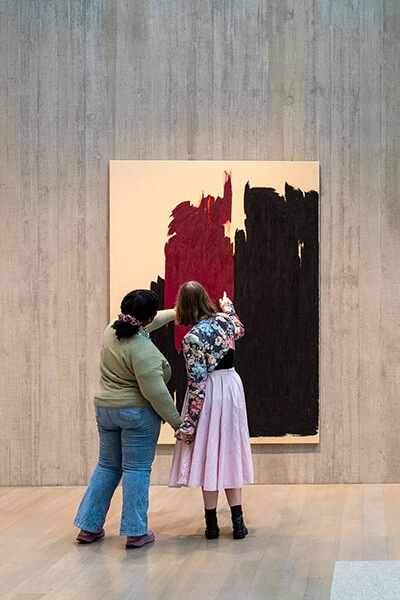 Two people hold hands and point at a painting