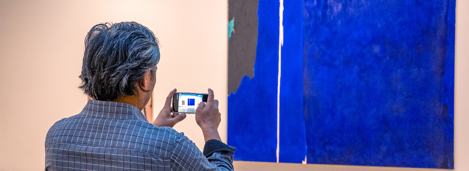 A man takes a photo of a large blue painting with his phone