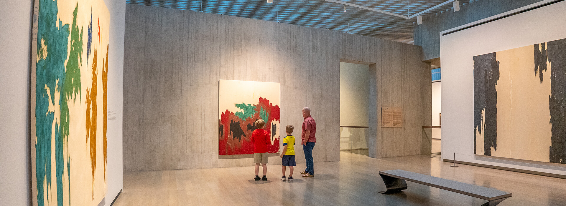 A father and his two sons look at a large abstract painting