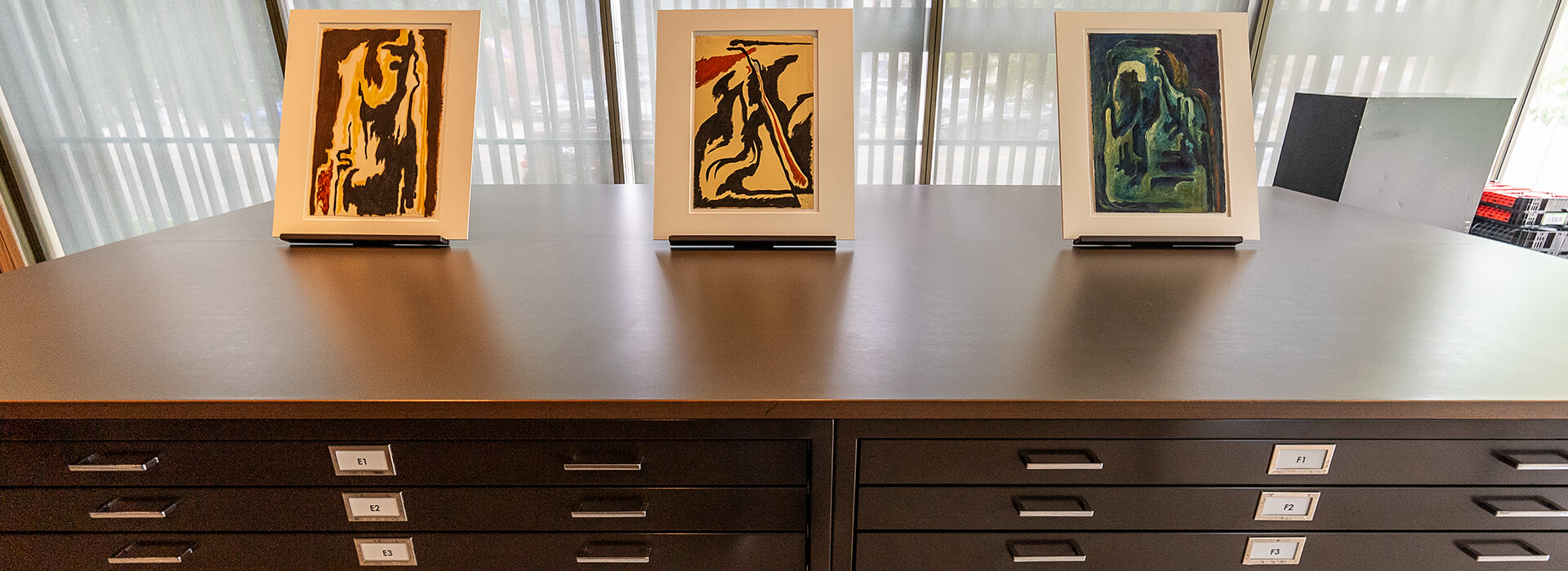 Three works on paper sit on top of file drawers