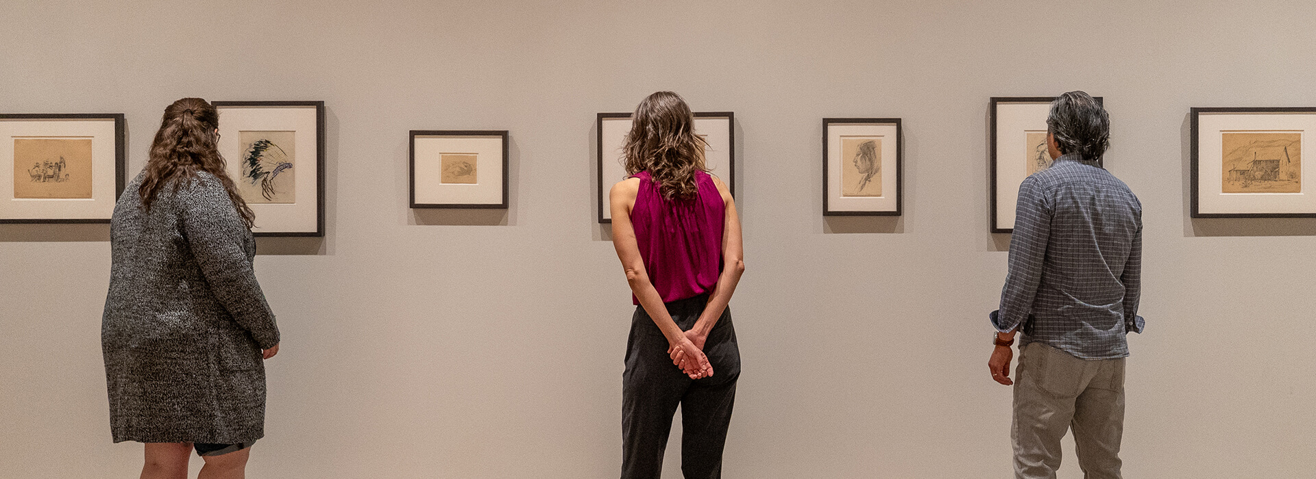 Three people look at small framed works on paper