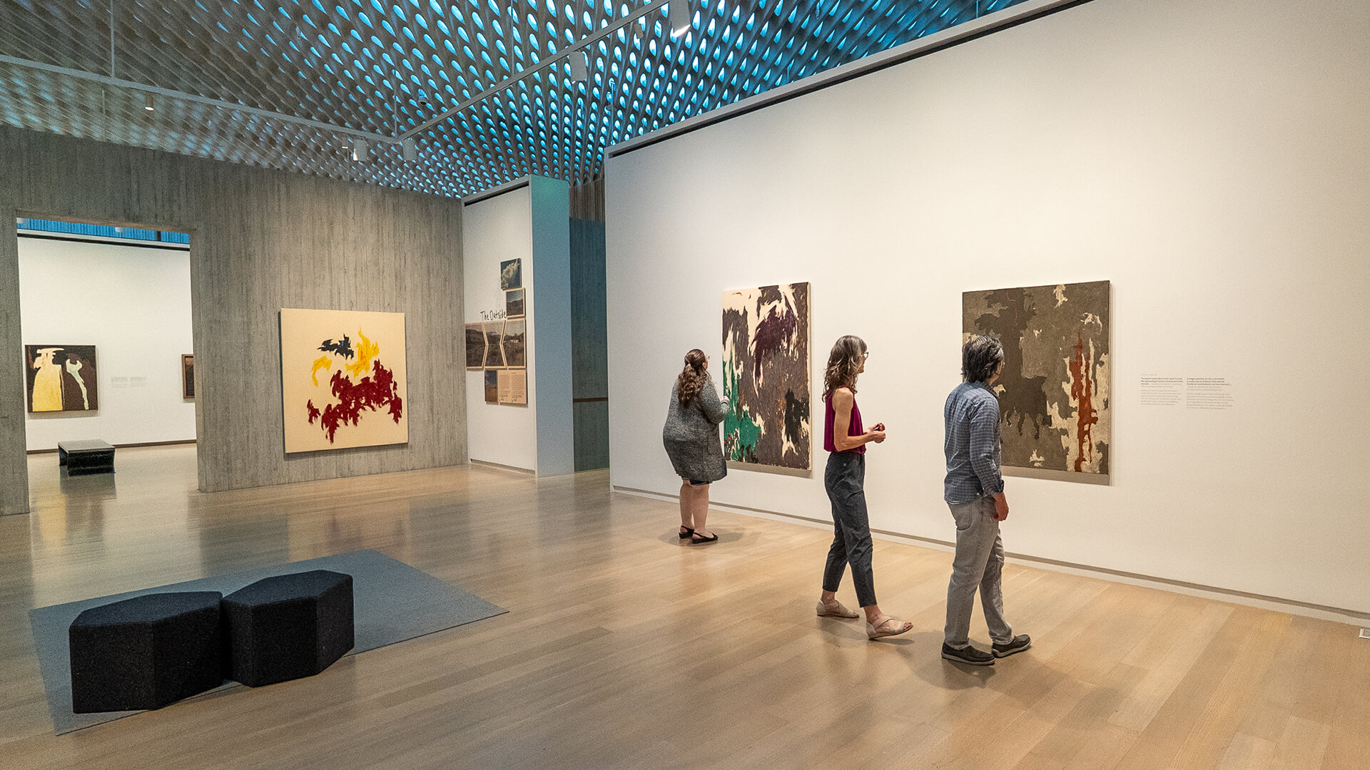Two women and a man each look at abstract Clyfford Still paintings on the walls of a gallery
