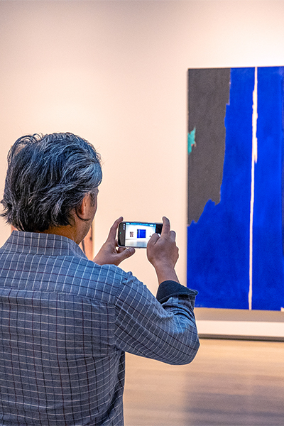 A man takes a photo of a large blue painting with his phone