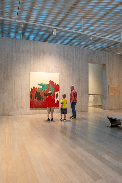 A father and his two sons look at a large abstract painting
