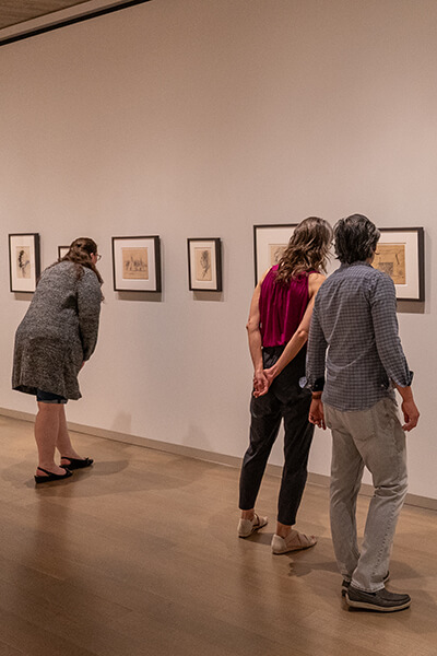 Three people look at small framed works on paper