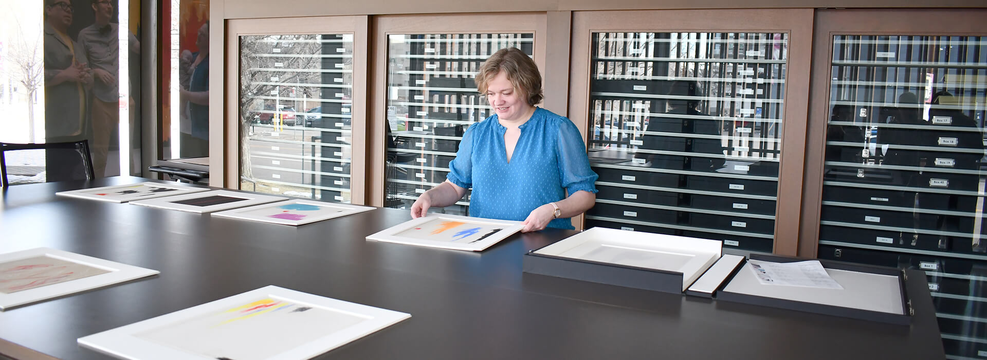 A woman looks at artworks on paper in matted frames