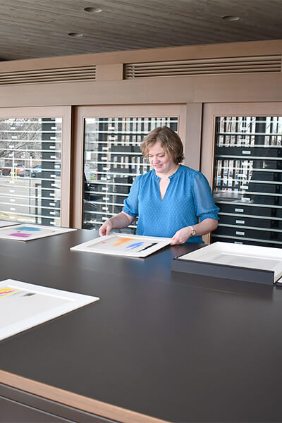 A woman looks at artworks on paper in matted frames