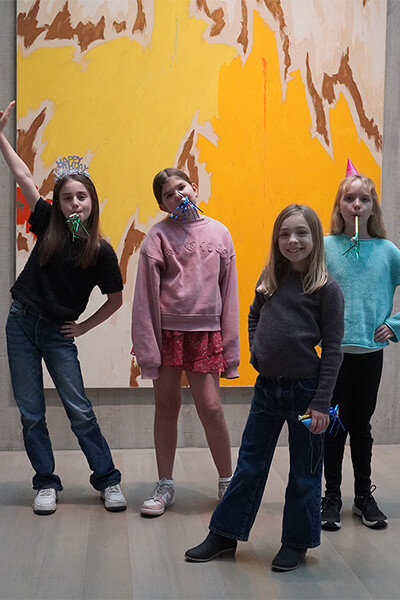 Four school-age girls pose in front of a painting wearing party hats