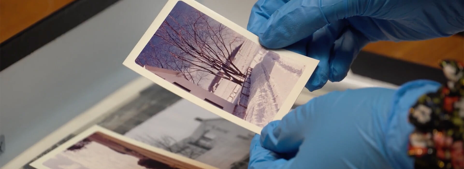 A woman wearing blue gloves holds an old photo of a snowy scene