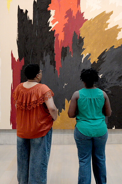 Two women look at a large colorful painting
