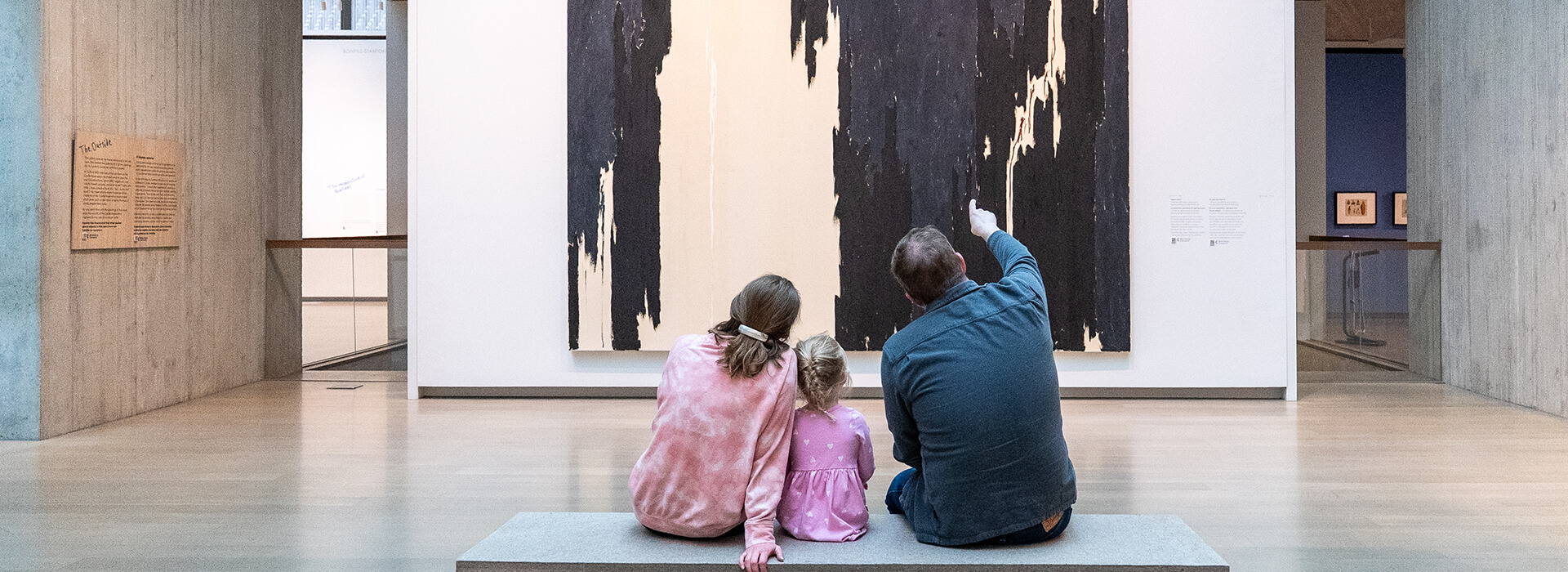 A family sits on a bench and looks at a large painting