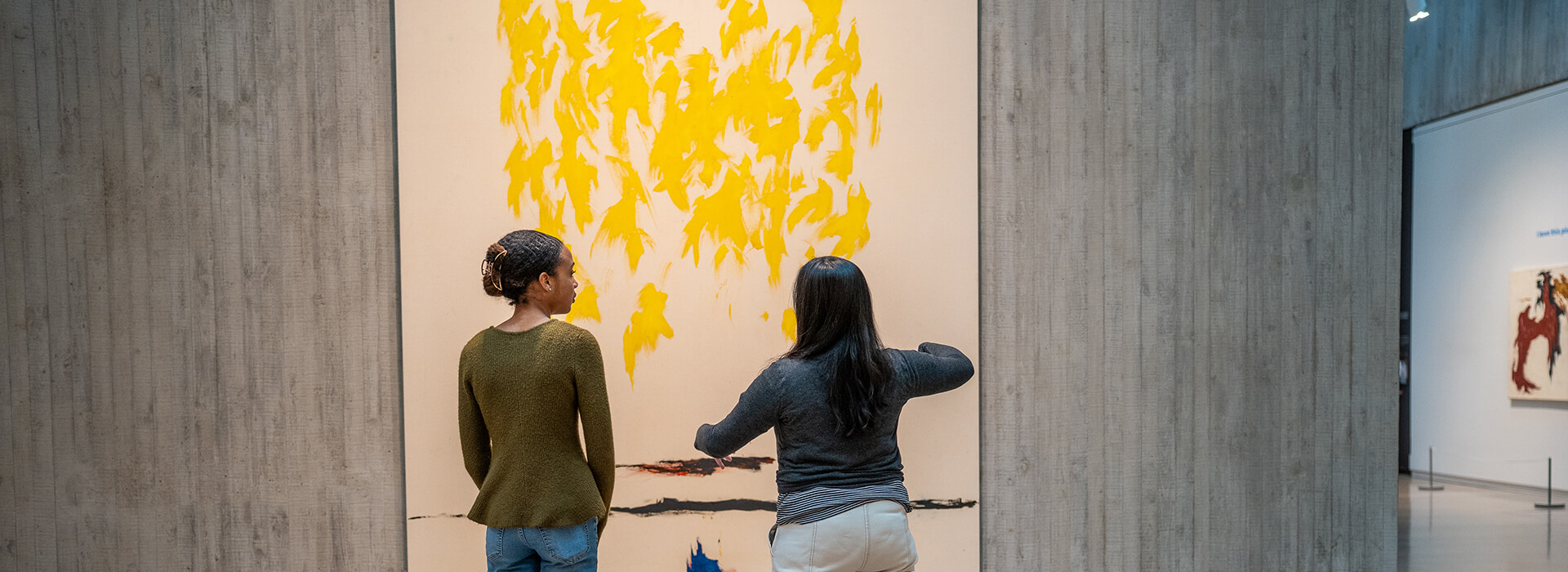 Two women look at a large yellow abstract painting