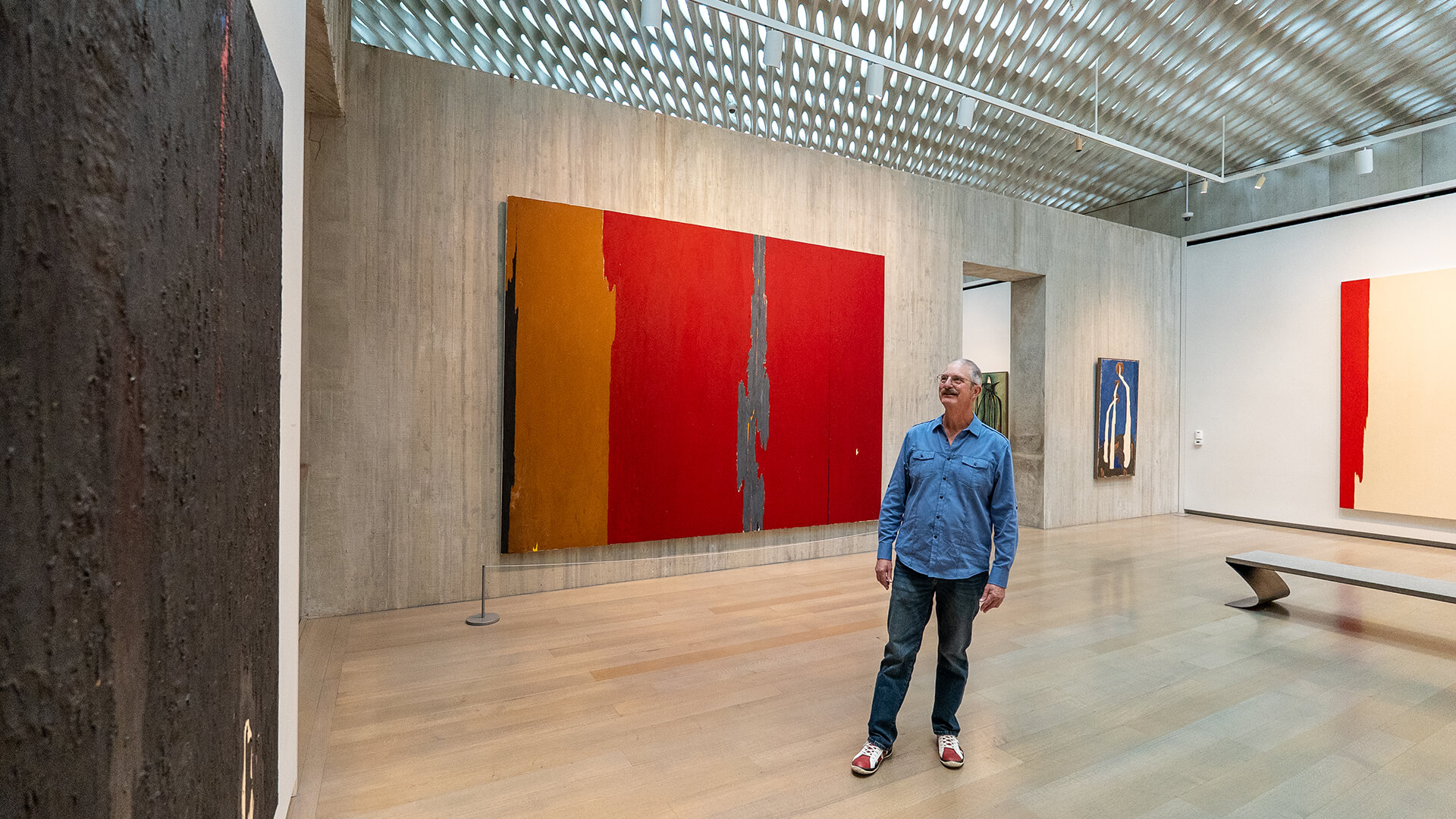 A man stands and looks at a large black abstract painting