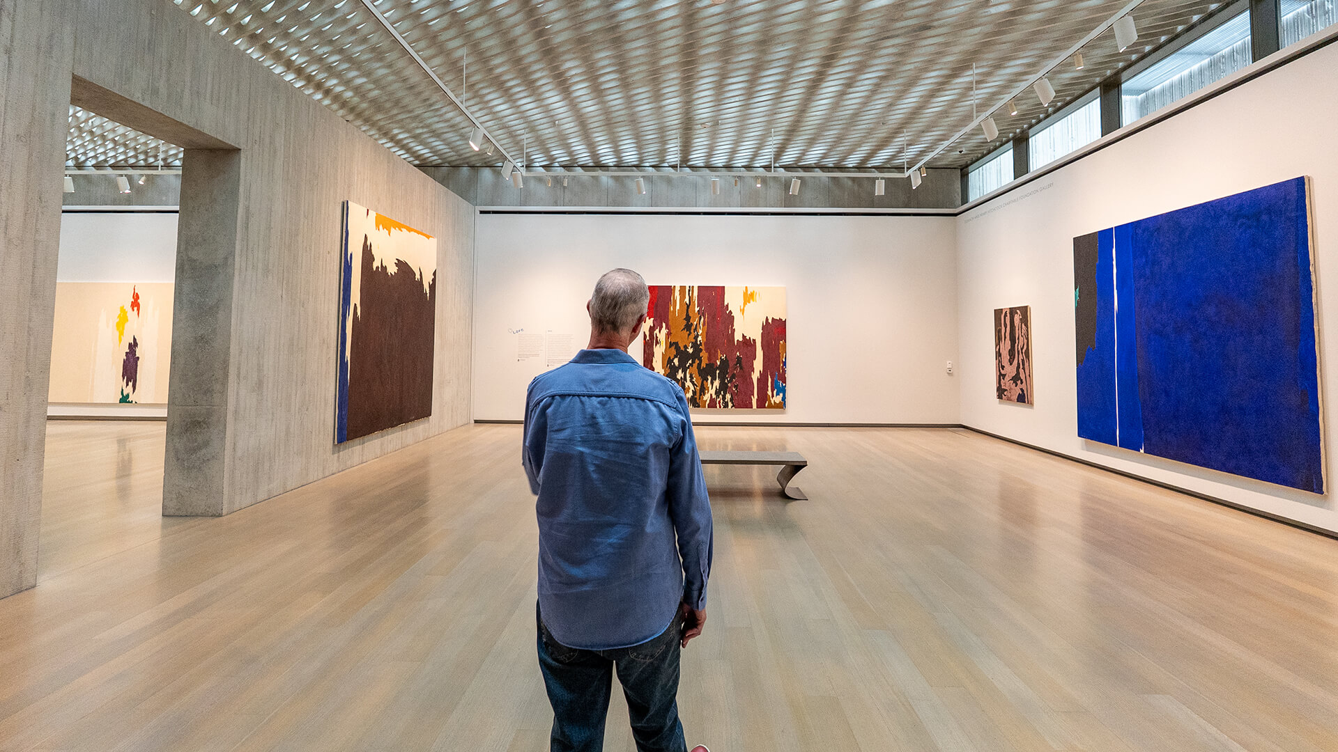 A man looks at a large gallery with abstract paintings