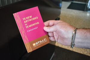 A person holds up a 15 new paintings in 15 months passport