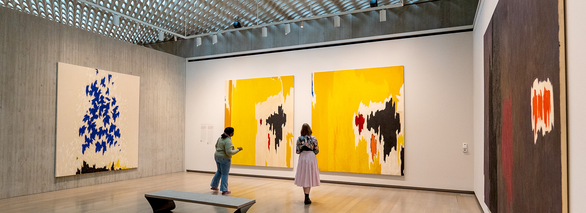 Two people look at abstract yellow paintings