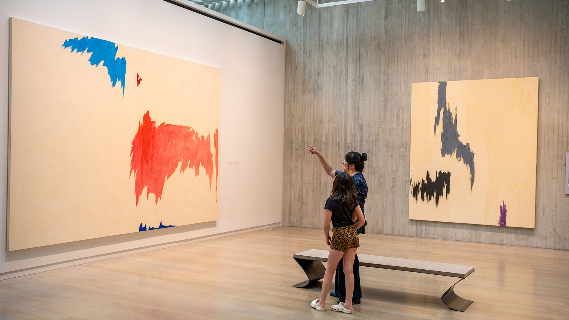 A mother and her daughter look at a large abstract painting with pink and blue shapes