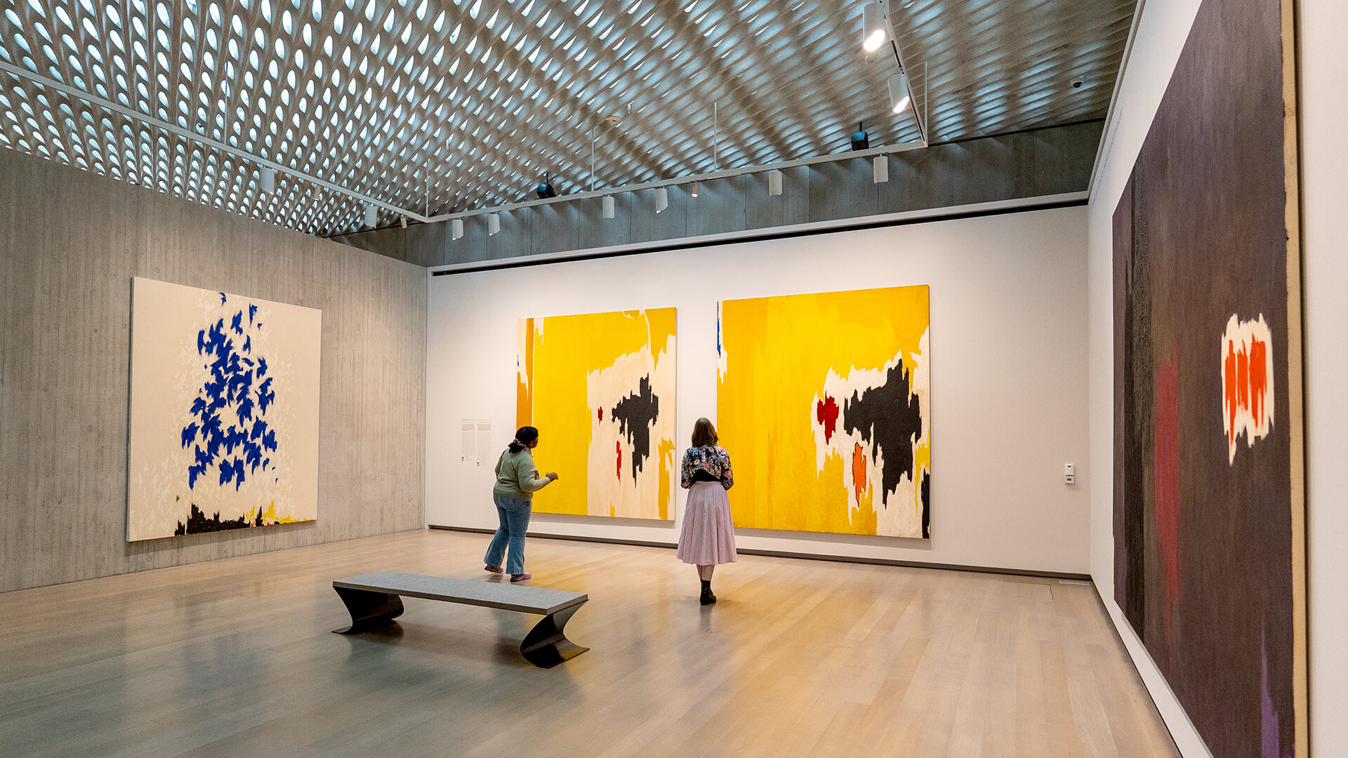 Two people look at abstract yellow paintings