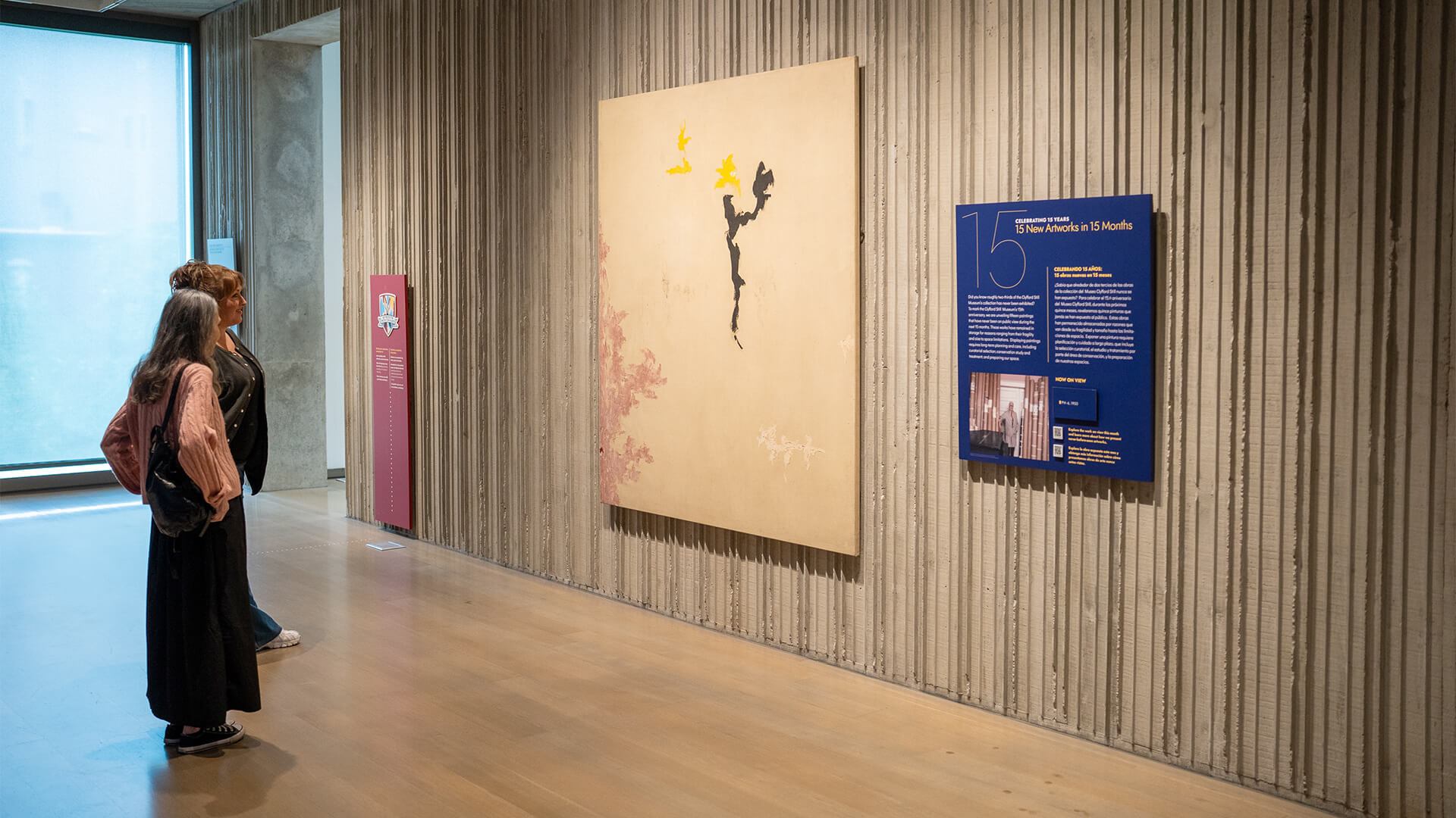 Two women look at an abstract painting on the wall