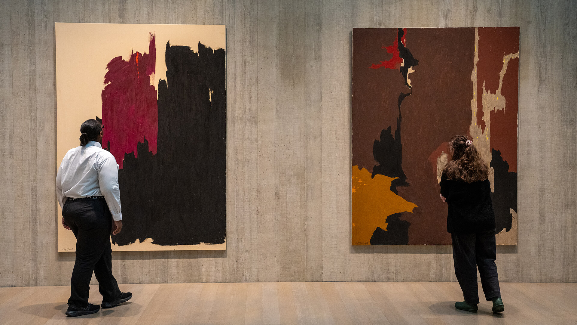 Two women look at two large abstract paintings on the wall