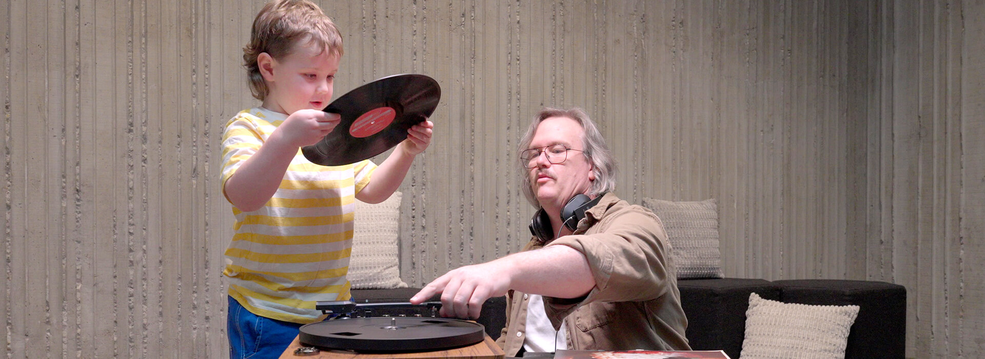 A child holds a record as the child's father points to the record player