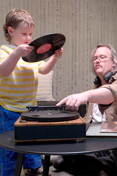 A child holds a record as the child's father points to the record player