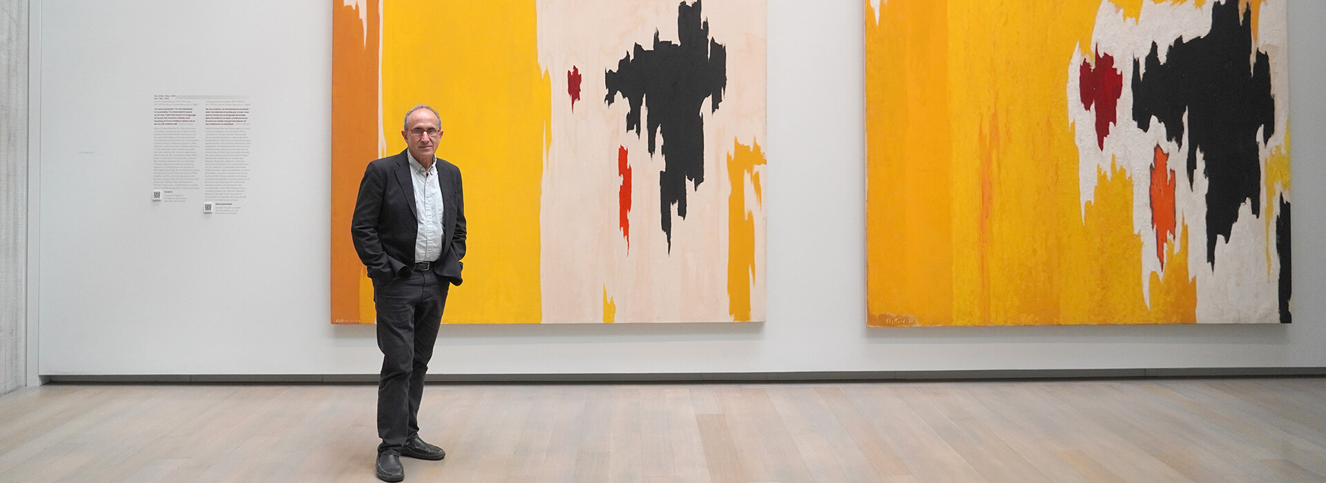 Harry Cooper stands in front of two abstract yellow, white and black paintings