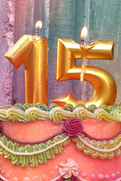 A colorful cake has gold 15 candles burning on top of it