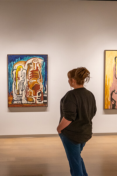 A woman looks at a painting of two abstracted figures