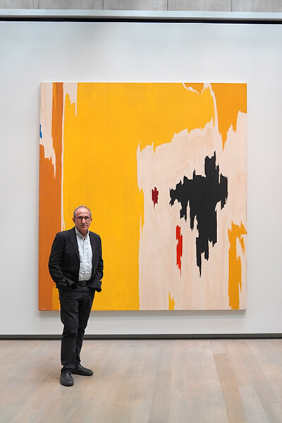 Harry Cooper stands in front of an abstract yellow, white, and black painting