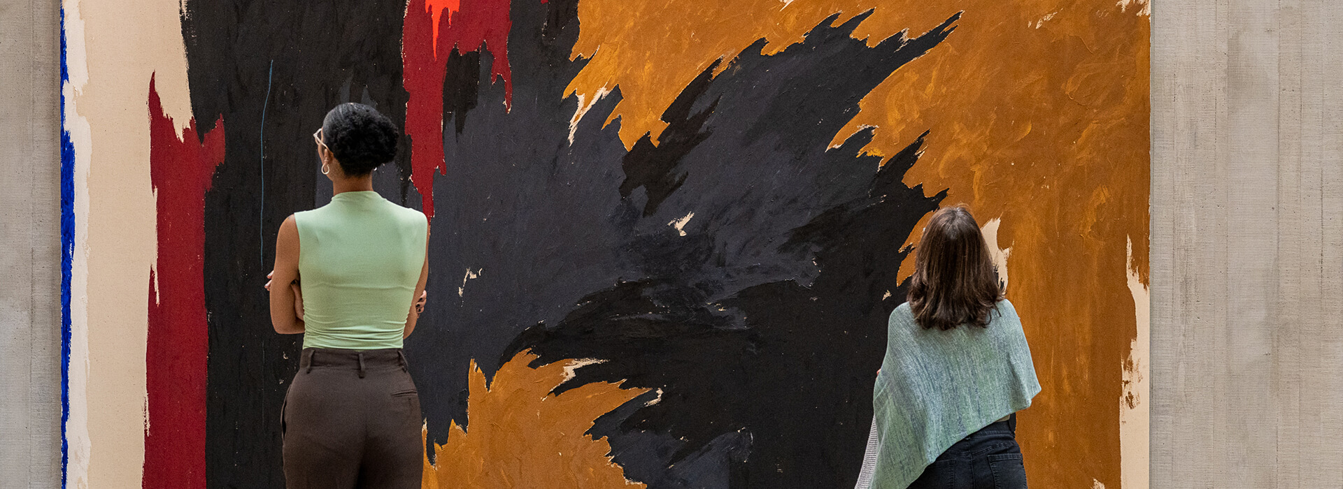 Two women look at a large colorful abstract artwork