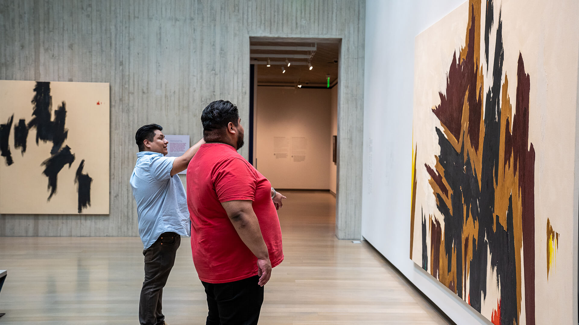 Two men look at a large brown and black abstract painting